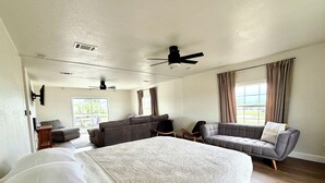 A spacious bedroom with a large bed, two sofas, a ceiling fan, and a view of the outdoors.