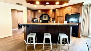A kitchen with wooden cabinets, a built-in microwave, a stove, and a refrigerator. There are three bar stools at the counter.