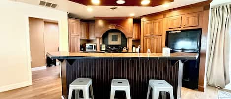 A kitchen with wooden cabinets, a built-in microwave, a stove, and a refrigerator. There are three bar stools at the counter.