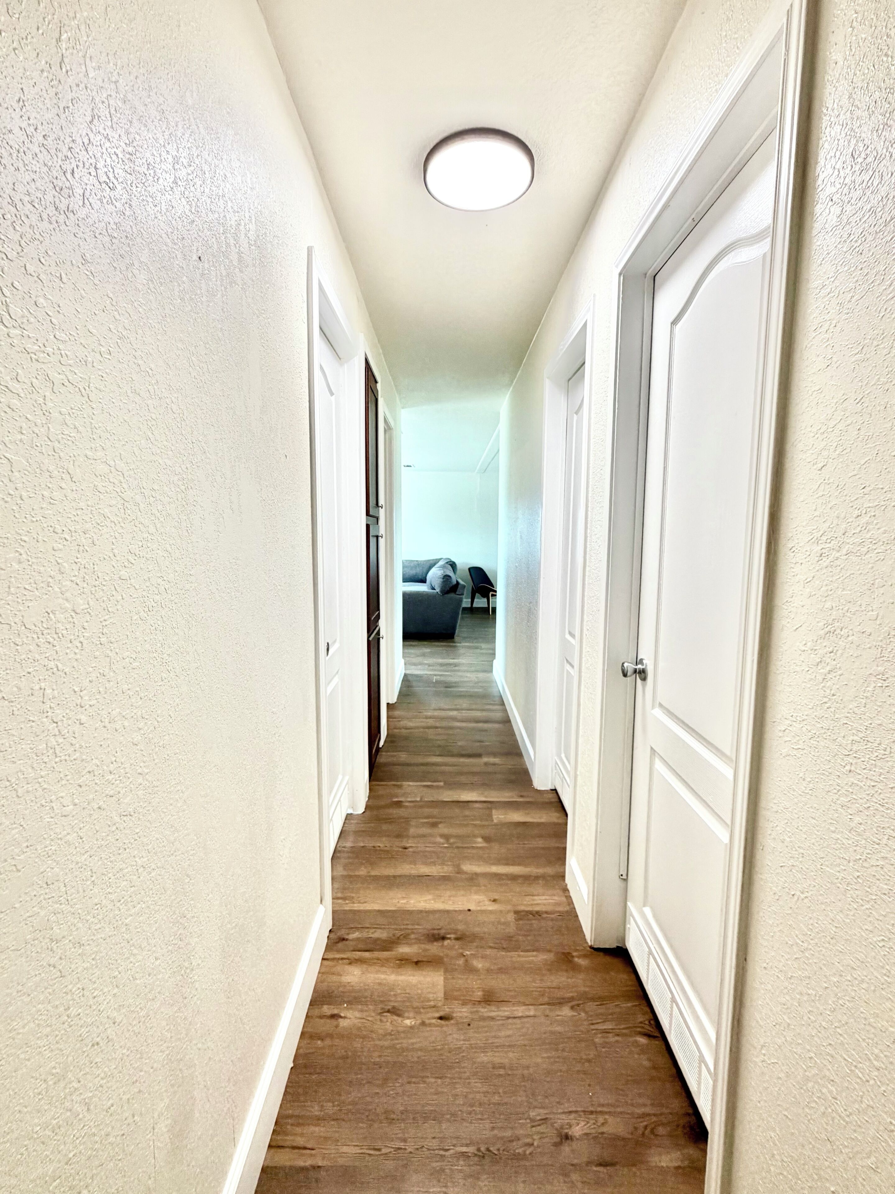 A narrow hallway with wooden flooring, white walls, and white doors.