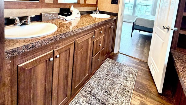 A bathroom with two sinks, a large mirror, wooden cabinets, a ceiling fan, and a rug.
