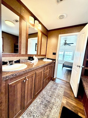 Un bagno con due lavandini, uno specchio grande, mobili impiallacciati in legno, una ventola a soffitto e un tappeto.