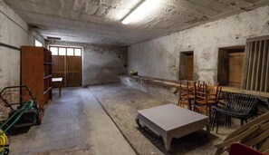 Ein Zimmer mit Betonboden, einem Holztisch, Stühlen, einer Bank und einer Holztür.