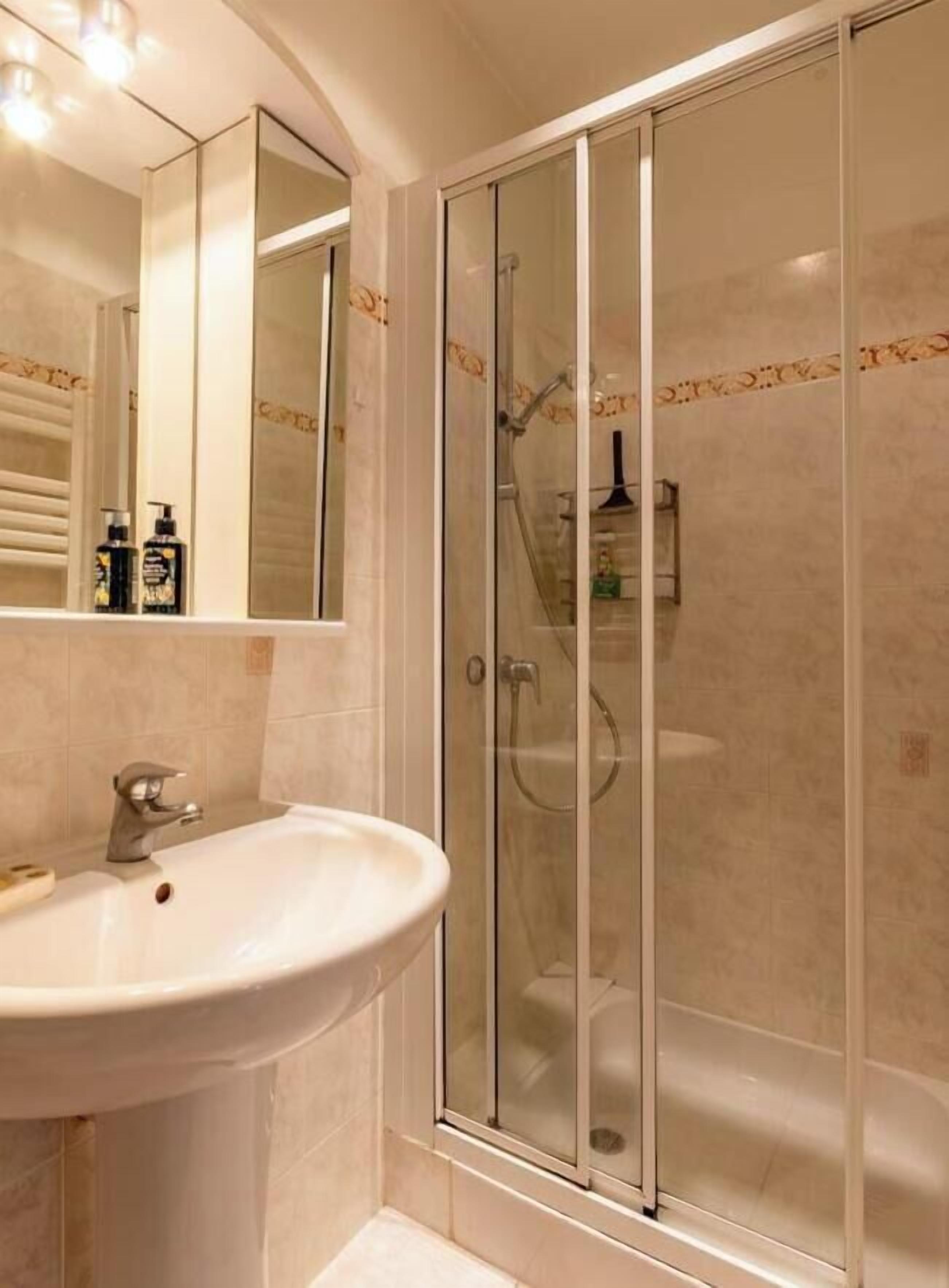 Ein Badezimmer mit einem weißen Waschbecken, einer Duschkabine aus Glas und einem Spiegel.
