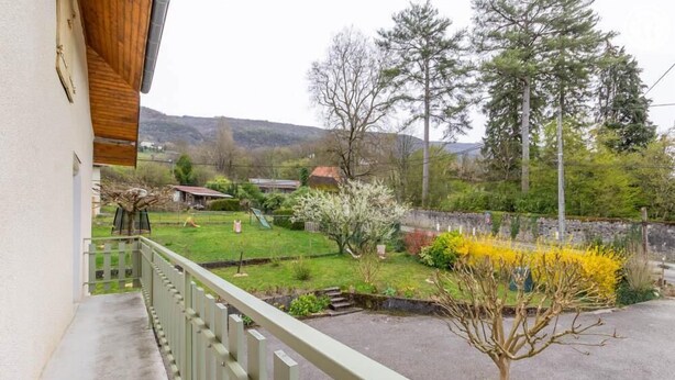En balkon med udsigt over en have, et lille træ og en bygning i det fjerne.
