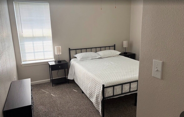 A bedroom with a bed, bedside tables, a window, and a carpeted floor.