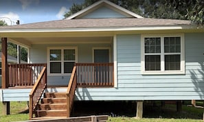A single-story house with a front porch, a staircase leading to the entrance, and a small deck area.