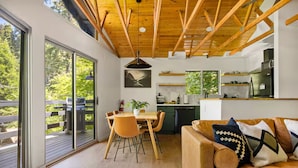 Una cocina moderna con vigas de madera, un comedor con mesa y sillas, y un sofá con cojines estampados.
