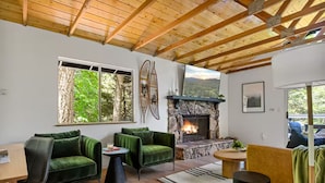 Una sala acogedora con chimenea, vigas de madera y un ventanal con vistas a la vegetación.