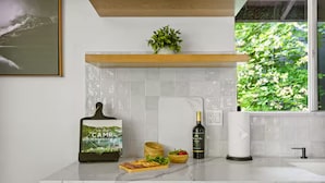 Una cocina con encimera de mármol, un mueble verde, una botella de vino y un libro de cocina.