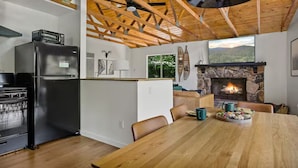 Una cocina moderna con horno empotrado, un refrigerador negro y una zona de comedor con mesa y sillas de madera.