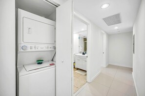 A laundry room with a washing machine, a dryer, and a small shelf with detergent containers. - Icon Brickell - 36th Floor - Ocean & City Views (Miami)
