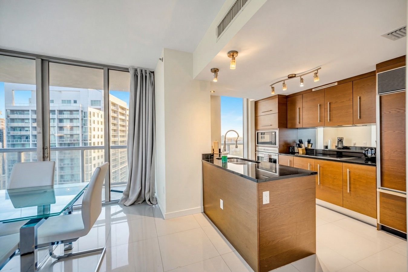 A modern kitchen with wooden cabinets, a central island, and a dining area with a glass table and chairs.