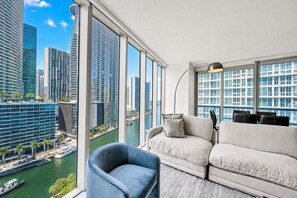 A modern living room with a large window, a sofa, a chair, and a lamp. - Icon Brickell 2BDR • 17th FL • Ocean & Pool Views (Miami)