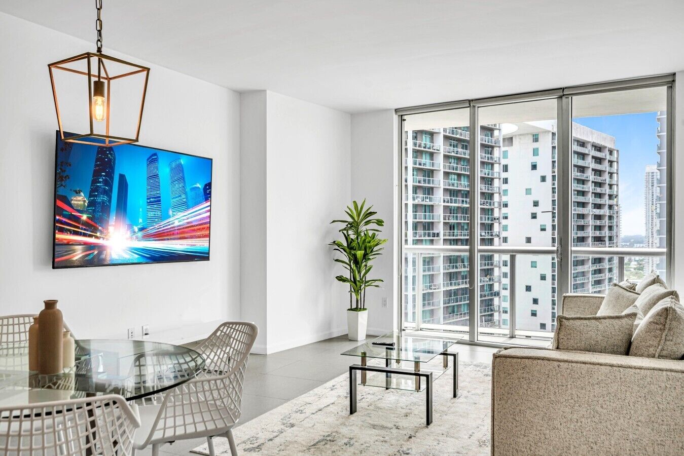 Een moderne woonkamer met een glazen tafel, witte stoelen, een bank, een potplant en een schilderij van een stadsgezicht.