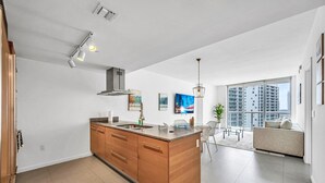 Una cocina moderna con una isla central, un comedor con sillas, un sofá y un amplio ventanal con vistas a la ciudad.