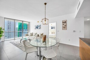 A modern living room with a glass dining table, white sofas, and a view of high-rise buildings. - Icon Brickell • 34th Floor • Ocean View • Free Spa (Miami)