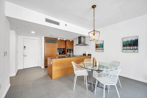 A modern kitchen with a central island, white chairs, and a glass dining table. - Icon Brickell • 34th Floor • Ocean View • Free Spa (Miami)