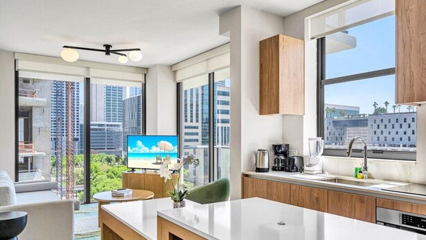 A modern kitchen with a large window, a flat-screen TV, and a dining area with a view of the cityscape.