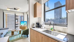 A modern hotel room with a kitchen, a dining area, and a large window with a city view.