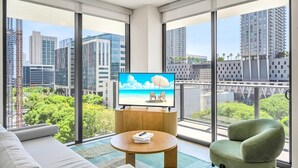 A modern living room with a large TV, a sofa, a coffee table, and a chair, with a city view through large windows.