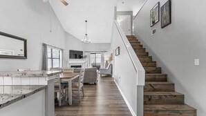 A modern kitchen with a granite countertop, wooden dining table, and chairs. A staircase with wooden steps leads to a landing with a door. - 3BR/3BA at Pointe Royale - Golf, Pools & Dining (Branson)