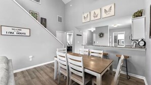 A modern kitchen with a central island, white cabinetry, and a dining area with a wooden table and chairs. - 3BR/3BA at Pointe Royale - Golf, Pools & Dining (Branson)