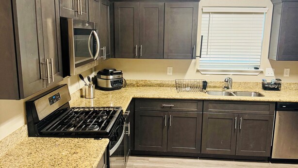 A modern kitchen with dark cabinets, a granite countertop, a built-in microwave, a stove, and a window with blinds.