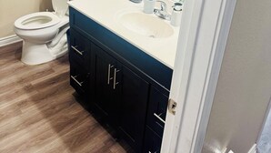 A bathroom with a toilet, sink, mirror, and dark cabinets.