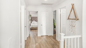 A hallway with white walls, wooden flooring, and white doors leading to a bedroom with a tufted headboard. - Serene 3-bedroom house with Tesla Charger in Ladera Ranch (Mission Viejo)