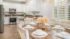 A modern kitchen with white cabinetry, stainless steel appliances, a dining table set for six, and a decorative vase. - Serene 3-bedroom house with Tesla Charger in Ladera Ranch (Mission Viejo)