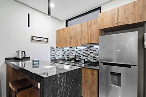 Eine moderne Küche mit Edelstahl-Kühlschrank, Holzschränken, einer schwarzen Marmorarbeitsplatte und einer gefliesten Spritzschutzwand.