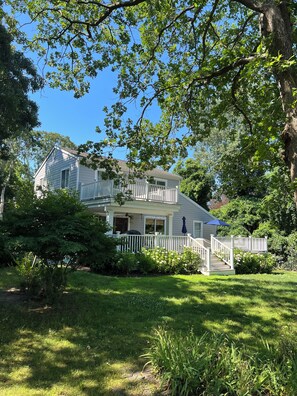 A two-story house with a porch, a white fence, and a staircase leading to the second floor. - Peconic Bay Cottage (Hampton Bays)