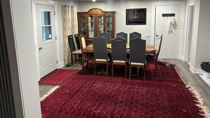 Ein Esszimmer mit Holztisch, Stühlen, einem roten Teppich mit Muster und einer Holzvitrine mit Glastüren.
