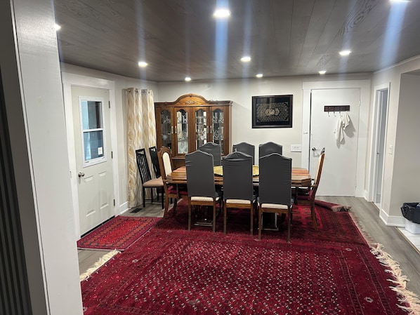 Comedor con mesa de madera, sillas, alfombra roja estampada y aparador de madera con puertas de cristal.