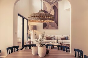 A dining area with a round wooden table, two white ceramic vases with branches, and a woven pendant light. - Luxury 5BR Villa - Hacienda Pinilla - Pool, Beach Club, Breakfast, House Keeping (Tamarindo)