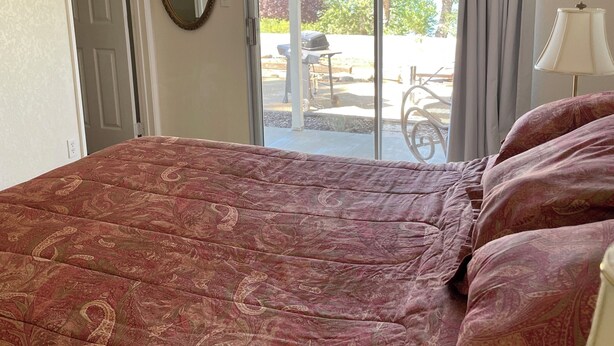 A bedroom with a large bed, a sliding glass door to a patio, and a lamp on the right side.