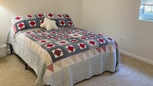Een slaapkamer met een bed, nachtkastje, raam met jaloezieën en foto's aan de muur.