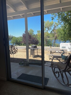 A covered patio with a view of a lake, outdoor furniture, and a grill.