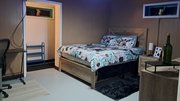Ein Schlafzimmer mit Bett, Schreibtisch, Stuhl, Lampe, einer Flasche und einem Fenster.