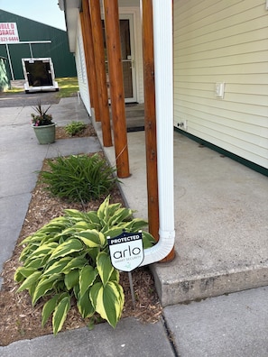 A house with a covered porch, a security sign, and a potted plant. - The Cottage at Midpoint. Charming 3 bedroom retreat near Higgins Lake. (Roscommon)