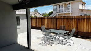 Un patio con una mesa y sillas, una valla de madera y un edificio con balcón al fondo.