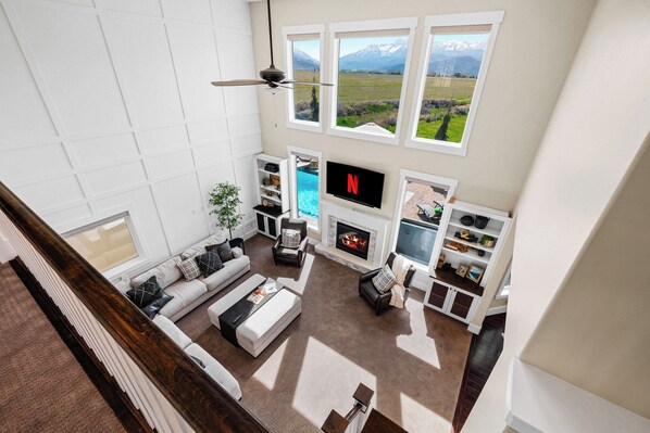 A spacious living room with a fireplace, a TV, and a view of a mountainous landscape through large windows.