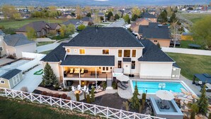 A large two-story house with a swimming pool, a covered patio, and a fenced backyard. - Ultimate Family Retreat: VIEWS, Sport Court, Theater, Pool, Sauna, Game Zone! (Heber City)