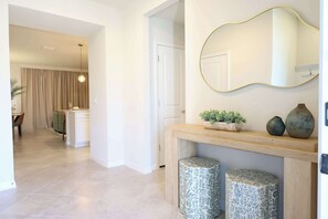 Een modern interieur met een houten console tafel, twee gestreepte krukken, een grote spiegel en een deur naar een andere kamer.