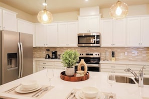 A modern kitchen with white cabinets, stainless steel appliances, a central island with a plant, and pendant lighting. - Modern 5BR Home with Game Room and Pool at Windsor Cay Resort (Clermont)