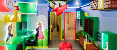 A colorful room with a Mario-themed desk, a red bean bag, and a television.
