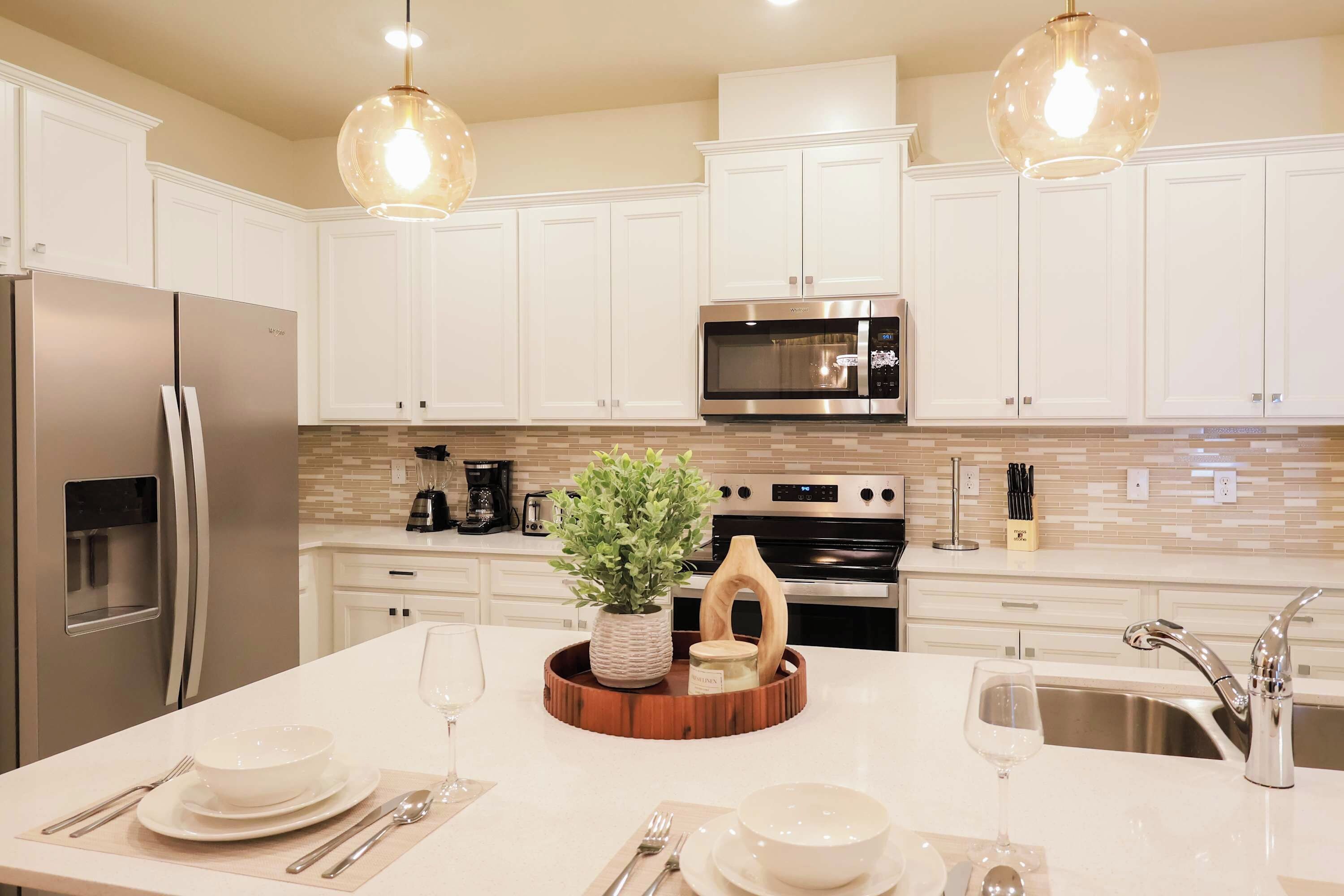 A modern kitchen with white cabinets, stainless steel appliances, a central island with a plant, and pendant lighting.