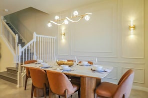 A dining area with a table set for four, white walls, a staircase, and a chandelier. - Modern 5BR Home with Game Room and Pool at Windsor Cay Resort (Clermont)