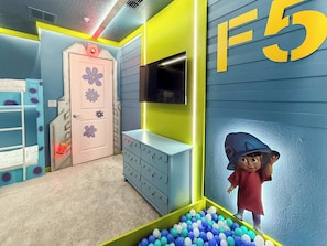 A child's playroom with a bunk bed, a pink door with flower decals, a TV on the wall, and a ball pit. - Modern 5BR Home with Game Room and Pool at Windsor Cay Resort (Clermont)